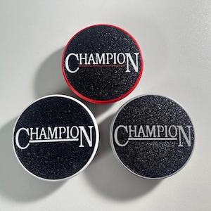 May include: Three round black and white phone grips with the word "CHAMPION" printed in white on each. One grip has a red border.