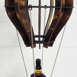 Könnte beinhalten: Ein Holz-Heißluftballon-Likörspender mit vier Schnapsgläsern und einem Flaschenhalter. Der Ballon ist braun und hat silberne Ketten.