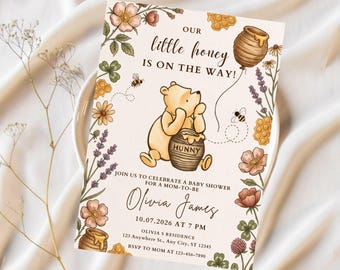 Puede incluir: Una tarjeta de invitación rectangular para baby shower con un oso amarillo que sostiene un tarro de miel etiquetado HUNNY, rodeado de flores, abejas y panales. El texto dice OUR little honey IS ON THE WAY! JOIN US TO CELEBRATE A BABY SHOWER FOR A MOM-TO-BE Olivia James 10.07.2026 AT 7 PM OLIVIA S RESIDENCE 123 Anywhere St., Any City, ST 12345 RSVP TO MOM AT 123-456-7890.
