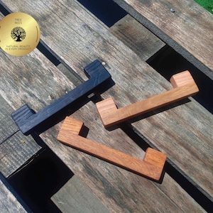 May include: Three wooden drawer pulls in varying shades of brown and black are displayed on a weathered wooden surface. The pulls have a rectangular design with a handle. A gold sticker with the text "TREE BEES NATURAL BEAUTY IN EVERY PRODUCT" is in the upper left corner.