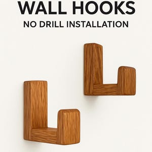 May include: Two wooden wall hooks with a natural wood grain finish. The hooks are L-shaped and mounted on a white background. Text at the top reads "WOODEN WALL HOOKS" and below that "NO DRILL INSTALLATION."