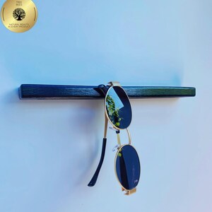 May include: A black wooden shelf with gold-framed sunglasses hanging from it. The sunglasses have dark lenses. A gold circular logo with the text "TREE BEES" and "NATURAL BEAUTY IN EVERY PRODUCT" is in the upper left corner.