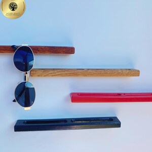 May include: A display of sunglasses on a wooden wall shelf. The shelf is made of different types of wood and painted in various colours, including red and black. The sunglasses have a gold frame and dark blue lenses. The image also includes a gold sticker with the text "TREE BEES".