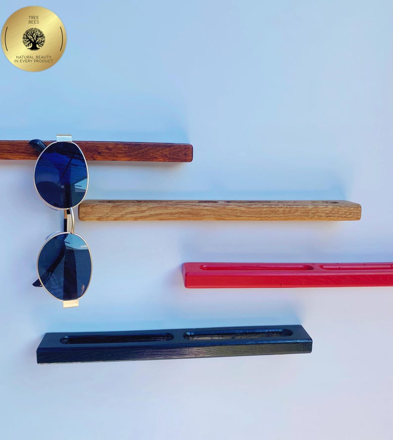 May include: A display of sunglasses on a wooden wall shelf. The shelf is made of different types of wood and painted in various colours, including red and black. The sunglasses have a gold frame and dark blue lenses. The image also includes a gold sticker with the text "TREE BEES".