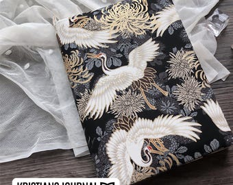 May include: A black journal cover with a gold and white floral pattern featuring cranes. The cover has a subtle sheen and a textured feel.