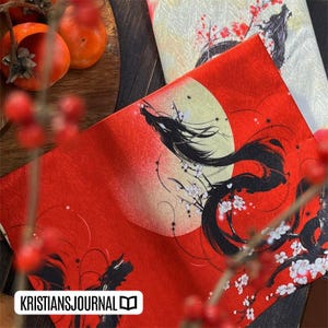 K&ouml;nnte beinhalten: Dekorativer Stoff in Rot und Creme mit japanisch inspiriertem Design. Der rote Stoff zeigt eine schwarze Drachenillustration mit Vollmond und Kirschbl&uuml;ten. Der cremefarbene Stoff hat ein &auml;hnliches Design. Der Text "KRISTIANSJOURNAL" ist sichtbar.