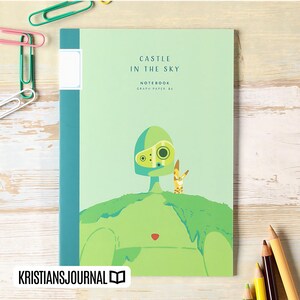May include: A light green notebook with the text "CASTLE IN THE SKY" and "NOTEBOOK GRAPH PAPER 86". The cover features a cartoon illustration of a green figure and a small yellow creature. The notebook has a teal spine and a white label.