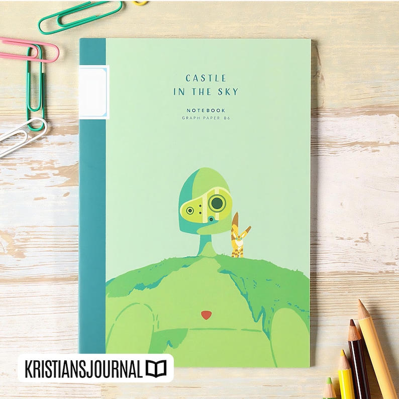 May include: A light green notebook with the text "CASTLE IN THE SKY" and "NOTEBOOK GRAPH PAPER 86". The cover features a cartoon illustration of a green figure and a small yellow creature. The notebook has a teal spine and a white label.