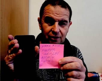 May include: A man holds a pink sticky note with the text "Mrez Kovac, Fomana, Jaroslav, Domank, Fidaras" written in purple ink.