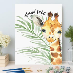 Puede incluir: Pintura a la acuarela de una jirafa con manchas marrones, ojos grandes y cuello largo. La jirafa está parcialmente oculta por hojas de palma verdes. Las palabras "Stand Tall" están escritas en escritura negra sobre la cabeza de la jirafa. Pinceles y botes de pintura en primer plano.
