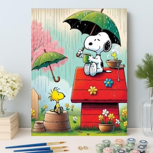 Puede incluir: Una pintura colorida de Snoopy y Woodstock bajo la lluvia. Snoopy, con una taza, está sentado en una caseta roja bajo un paraguas verde. Woodstock está en un barril de madera. El fondo presenta un árbol rosa y flores.