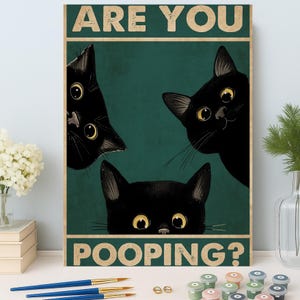 Op de afbeelding: Een rechthoekige wandkunstprint met drie zwarte katten met gele ogen die achter een donkergroene achtergrond vandaan kijken. De tekst "ARE YOU POOPING?" is in het wit bovenaan en onderaan gedrukt.