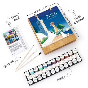 Puede incluir: Un kit de calendario de escritorio DIY con base de madera, que mide 18,2 cm de ancho y 22,5 cm de alto. El calendario presenta una ilustración colorida y el año 2026. Incluye botes de pintura, pinceles y una tarjeta de colores.
