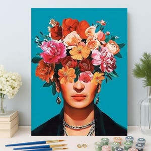 May include: A paint-by-numbers kit featuring a portrait of a woman with a floral headdress. The artwork has a teal background and includes paintbrushes, paint pots, and a canvas. The woman's face is visible, with a necklace and earrings.