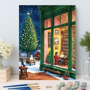May include: A winter scene paint-by-numbers kit. The image shows a Christmas tree, a snowman, and a person reading in a cozy room. The scene is set in a snowy environment with a green building and a warm interior. Paintbrushes and paint pots are in the foreground.