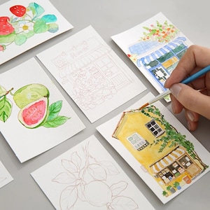 May include: Watercolour paintings of a strawberry plant, guava fruit, a flower shop, and a yellow house with a striped awning. A hand holds a paintbrush, adding details to the house painting. The paintings are on white paper.