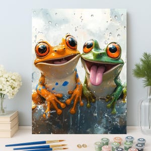 May include: A colorful painting of two cartoon frogs. One frog is orange with blue spots, and the other is green. Both frogs have large, expressive eyes and are smiling. The green frog has its tongue sticking out. The background is a light blue with water droplets.