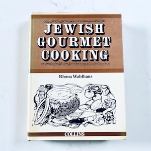 May include: A hardback book titled Jewish Gourmet Cooking by Rhona Wahlhaus, published by Collins. The cover features a tan upper section with dark blue text and a white lower section with a detailed black ink illustration of kitchen tools.