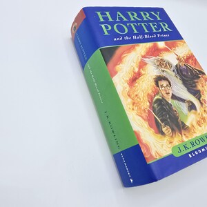 May include: A blue and green hardcover book with the title "Harry Potter and the Half-Blood Prince" on the cover. The cover features an illustration of Harry Potter and Albus Dumbledore in a fiery scene.