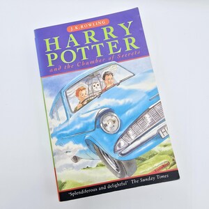 May include: A blue book cover with the title "Harry Potter and the Chamber of Secrets" by J.K. Rowling. The cover features an illustration of a blue car flying through the air with a white owl and two people inside.