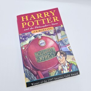 May include: A red and black book cover with the title "Harry Potter and the Philosopher's Stone" by J.K. Rowling. The cover features an illustration of the Hogwarts Express train and a young boy with glasses.