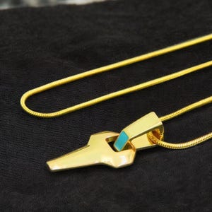 May include: A gold chain necklace with a geometric pendant featuring a turquoise inlay. The pendant is shaped like a key.