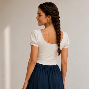 May include: A cream-colored short-sleeved top with a scoop neckline and a fitted bodice, paired with a solid dark navy blue skirt. The top features puff sleeves and a clean, simple design, while the skirt has a smooth, flowing silhouette.
