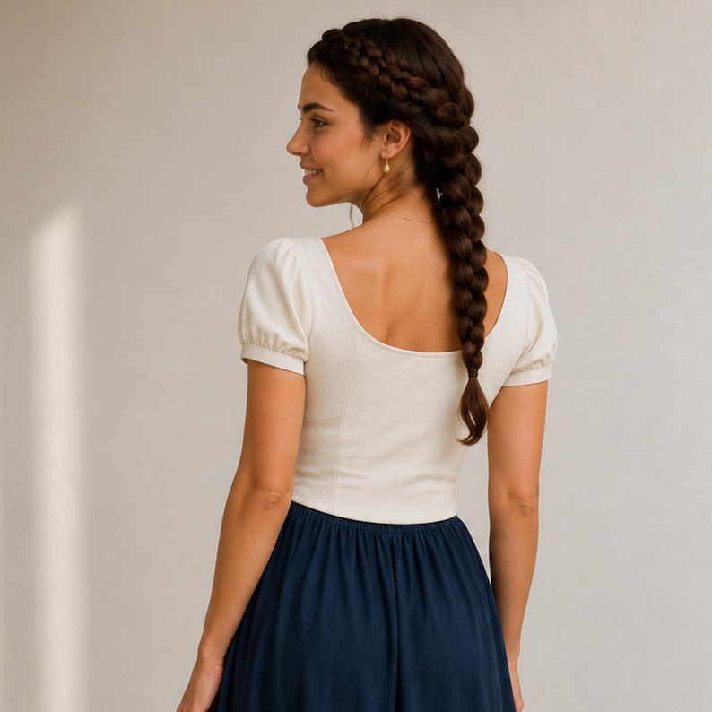 May include: A cream-colored short-sleeved top with a scoop neckline and a fitted bodice, paired with a solid dark navy blue skirt. The top features puff sleeves and a clean, simple design, while the skirt has a smooth, flowing silhouette.
