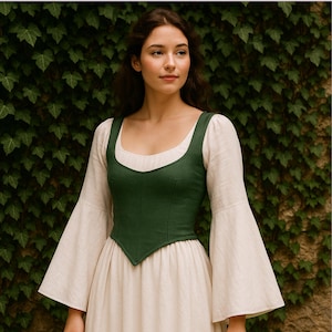May include: A woman wearing a medieval-style outfit. The ensemble includes a dark green bodice, a cream-colored dress, and long, bell-shaped sleeves. The background is a wall covered in green ivy.