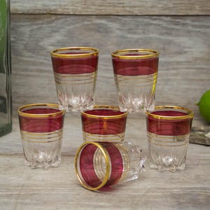 May include: Set of six clear glass shot glasses with a gold rim and a burgundy band around the middle.