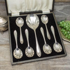 Peut inclure: Un ensemble de cuillères de service et de petites cuillères en argent ancien, présenté dans un coffret doublé de velours noir. Les cuillères présentent un motif en forme de coquillage sur les cuillères et des détails ornés sur les manches.