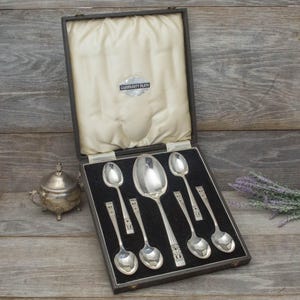May include: A set of silver spoons presented in a black box with a cream satin lining. The box is labelled "Community Plate". A small silver sugar bowl is to the left of the box.