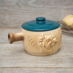 May include: A ceramic pot with a teal lid and a brown handle. The pot has a relief design of a cow's head and the word "Beef" on the side.