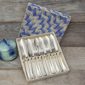 May include: A set of ten silver-plated fish forks and knives in a white box with a blue and white patterned lid. The box is open and the forks and knives are arranged in rows.