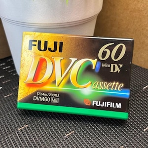 Può includere: Una cassetta Fuji DVC Mini DV. La scatola è dorata, nera e verde, con la scritta "FUJI DVC 60 Mini DV cassette" in bianco e giallo. La lunghezza del nastro è di 70,4 metri.