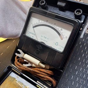Op de afbeelding: Een vintage zwart analoog elektrisch meetinstrument met een witte wijzerplaat met een gebogen schaal van 0 tot 75. Het apparaat toont tekst waaronder M45MOM3, 1978, 047458, 75mV en GOST 8711-60. Het bevat een opgerolde bruine draad met witte connectoren.