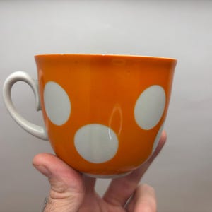 以下が含まれることがあります： 白い水玉模様のオレンジ色のセラミックマグカップ。