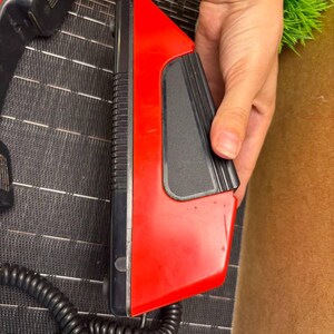 May include: A vintage red and black telephone receiver with a coiled cord. The receiver has a rectangular design with a black earpiece and a red body. The phone is likely from the 1980s or 1990s.