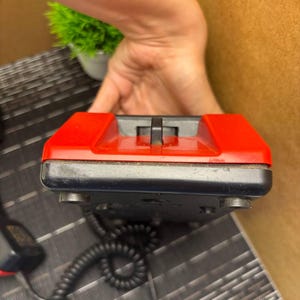 May include: A vintage black and red telephone with a coiled cord. The phone has a rectangular shape with a red top and a black base. The handset is not visible in the image.