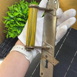 May include: Vintage door handle featuring a yellow and brown cylindrical grip and a rectangular metal plate. The plate has a keyhole and is connected to the grip with metal arms. The handle shows signs of age and wear.