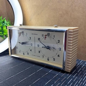 Può includere: Orologio da scacchi Jantar vintage con cassa color crema e due quadranti. L'orologio ha una cornice argentata e numeri neri. Il testo "MADE IN USSR" è visibile. Un classico per gli appassionati di scacchi.