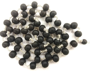 May include: A necklace featuring dark, matte black beads strung on a delicate silver chain. The beads are round and evenly spaced, creating a simple yet elegant design. The necklace is displayed against a white background.