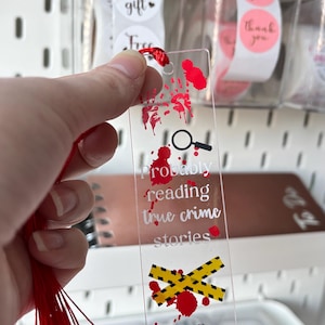 Op de afbeelding: Transparante acryl boekenlegger met rode kwast. De boekenlegger heeft een vergrootglas, bloedspatten, waarschuwingslint en een lichaamsomtrek. De tekst luidt "probably reading true crime stories."