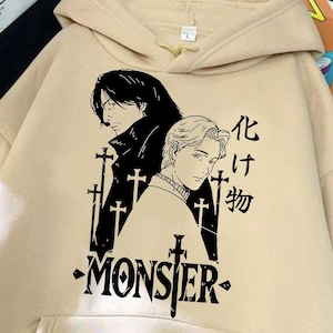 Może przedstawiać: Beżowa bluza z kapturem z przednią kieszenią i kapturem. Przód zdobi czarno-biała grafika dwóch postaci oraz napis "MONSTER" z japońskim tekstem. Bluza wykonana jest z miękkiego materiału.