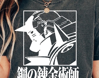 May include: Dark gray t-shirt featuring a white graphic of anime characters within a white rectangle. Japanese text and the words "FULLMETAL ALCHEMIST" are printed below the graphic.