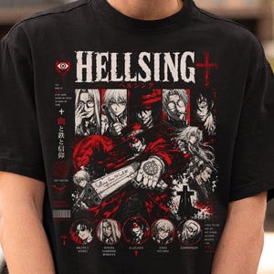 May include: A black t-shirt featuring a graphic print from the anime Hellsing. The design includes the title HELLSING in white, a central character holding a large handgun, multiple character portraits, red accents, and Japanese text characters.