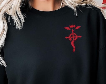 May include: Black sweatshirt with a red emblem on the upper left chest. The emblem is a stylized design with a central staff and wings. The sweatshirt is a solid black color and has long sleeves. A red rose is held in the lower left.