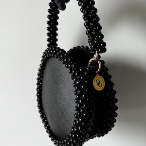 May include: A black round beaded handbag with a black beaded top handle and a gold circular tag with the letters "DG" on it.
