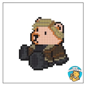 May include: Pixelated image of a bear-like character with blonde hair and a dark outfit. The character is in a seated position. A circular logo in the bottom right corner reads "SEW DEMICIOUS" with a cartoon bear holding a needle and thread.