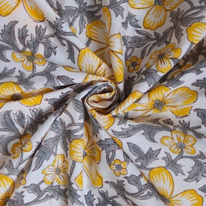 May include: White fabric with a repeating pattern of yellow flowers and gray leaves. The flowers have a detailed design, and the fabric is folded, creating shadows and depth.